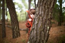 Male toddler wearing tiger suit hiding behind tree — Stock Photo