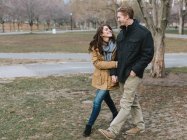 Young couple walking through park, arm in arm, smiling — Stock Photo