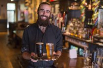 Портрет молодого бармена, несущего поднос с пивом в общественном доме — стоковое фото