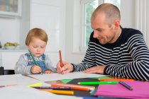 Mid adult man and toddler daughter drawing at kitchen table — Stock Photo