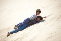 Two young boys lying on sandy hill, playing — Stock Photo