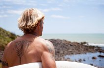 Вид ззаду зрілого чоловіка з дошкою для серфінгу на пляжі — стокове фото