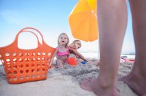 Kapstadt, Südafrika, zwei Kinder sitzen unter dem Sonnenschirm am Strand, während der Erwachsene neben ihnen steht — Stockfoto