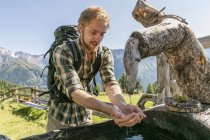 Jovem caminhante do sexo masculino bebendo água da calha rústica, Karthaus, Val Senales, Tirol do Sul, Itália — Fotografia de Stock