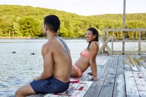 Young couple sitting on pier by lake, rear view — Stock Photo