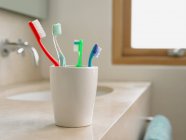 Cepillos de dientes de colores en la taza en el lavabo - foto de stock