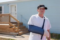 Man outside house with arm in sling — Stock Photo