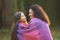 Mother and daughter wrapped in blanket in garden — Stock Photo