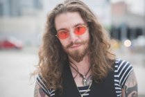Portrait de jeune hippie mâle aux lunettes de soleil orange et aux cheveux longs — Photo de stock
