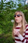 Woman blowing dandelion in park — Stock Photo