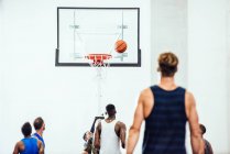 Rear view of male basketball team watching ball going into hoop on basketball court — Stock Photo