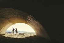 Surfing couple walking through beach underpass, Newport Beach, California, USA — Stock Photo