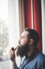 Молодий бородатий чоловік палить трубу біля вікна — стокове фото