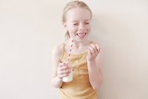 Young girl sticking tongue out and holding glass of milk — Stock Photo