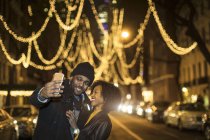 Casal feliz romântico desfrutando da cidade durante as férias de inverno tomando selfie na frente de luzes de férias — Fotografia de Stock