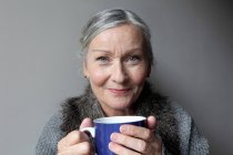 Пожилая женщина пьет кофе в помещении — стоковое фото