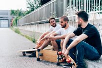 Side view of young men sitting on kerb with skateboards — Stock Photo