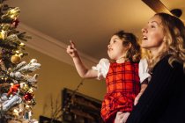 Niña con madre señalando la bola del árbol de navidad - foto de stock