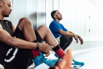 Exhausted male basketball players taking a break on changing room floor — Stock Photo
