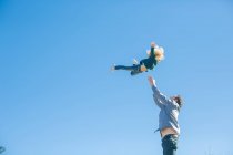 Menina sendo jogado no ar pelo pai contra o céu azul — Fotografia de Stock