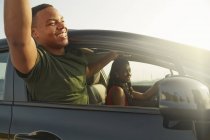 Young man leaning out of car window smiling, arms raised — Stock Photo