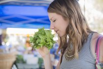Woman at fruit and vegetable stall smelling fresh herbs — Stock Photo