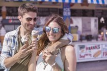 Casal contemporâneo ter um bom tempo no parque de diversões calçadão comer sorvete macio — Fotografia de Stock