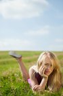 Молодая женщина лежит на фронте в поле, улыбаясь — стоковое фото