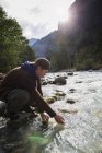 Male hiker crouching down by river, Lauterbrunnen, Grindelwald, Switzerland — Stock Photo