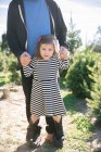 Portrait of small girl holding father's hands and standing on his feet by fir trees — Stock Photo