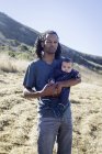 Ritratto di padre in piedi sulla spiaggia, con bambino in braccio — Foto stock