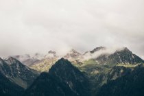 Rocky mountains with low clouds and sun lighted valley — Stock Photo