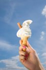 Mão feminina segurando sorvete com céu azul no fundo — Fotografia de Stock