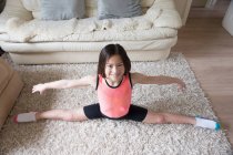 Menina praticando divisões de ginástica no tapete da sala de estar — Fotografia de Stock