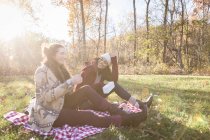 Две молодые женщины сидят на одеяле для пикника и смеются — стоковое фото