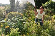 Жінка обприскує сад шлангом — стокове фото