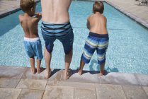 Rear view of man and two sons practicing diving poolside, Laguna Beach, California, USA — Stock Photo