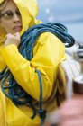 Woman in yellow raincoat and sunglasses carrying rope — Stock Photo