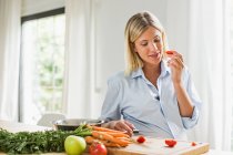 Full term pregnancy young woman eating tomato slice in kitchen — Stock Photo