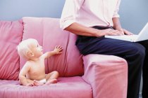 Bebê no sofá com homem digitando — Fotografia de Stock
