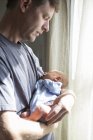 Padre sosteniendo bebé niño al lado de ventana - foto de stock