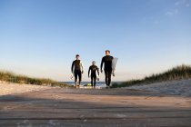 Tres surfistas caminando en el paseo marítimo - foto de stock