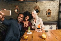 Multicultural Pessoas sorrindo tirando selfie no smartphone enquanto sentado no café — Fotografia de Stock