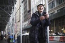 Человек, прислонившись к фонарику, смеясь, держит смартфон, Манхэттен, Нью-Йорк, США — стоковое фото