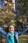 Chica lanzando hojas de otoño y sonriendo - foto de stock
