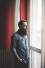 Молодий бородатий чоловік стоїть біля вікна — стокове фото