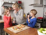 Mutter und zwei Töchter bereiten in der Küche Essen zu und knabbern an Zutaten — Stockfoto
