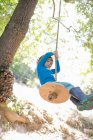 Young boy outdoors, swinging on rope swing — Stock Photo