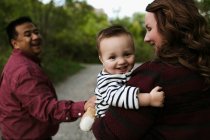 Baby Junge in den Armen der Mutter blickt lächelnd in die Kamera — Stockfoto