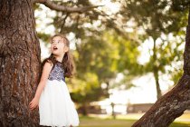 Retrato de niña apoyada en el tronco del árbol mirando hacia arriba - foto de stock